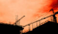 Are portfolios under-positioned for the rebuilding of the physical economy? Residential building development and construction, back lit cranes and scaffold with orange sky