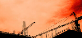 Residential building development and construction, back lit cranes and scaffold with orange sky