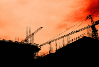 Residential building development and construction, back lit cranes and scaffold with orange sky