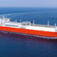 A large red and white freight ship takes a long turn in the flat, blue ocean