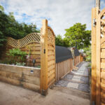 Property, home and exterior of backyard, entrance and door by architecture with walkway. Residential real estate, house or garden fence, trees or path by building patio outdoor on landscape in summer.