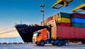 A containership unloads in a port as a articulated lorry truck carries off one of the cargo containers