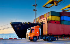 A containership unloads in a port as a articulated lorry truck carries off one of the cargo containers