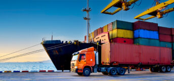 A containership unloads in a port as a articulated lorry truck carries off one of the cargo containers