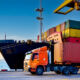 A containership unloads in a port as a articulated lorry truck carries off one of the cargo containers