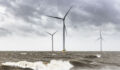 Wind turbines in an offshore wind park during a storm with big waves hitting the shore.