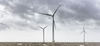 Wind turbines in an offshore wind park during a storm with big waves hitting the shore.