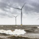 Wind turbines in an offshore wind park during a storm with big waves hitting the shore.