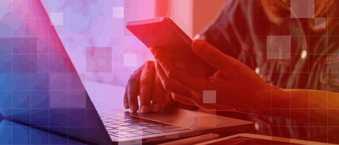 A person is reading their phone while sitting in front of a laptop