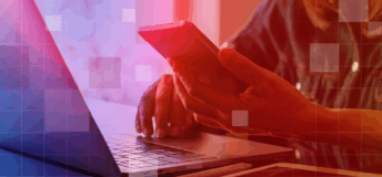 A person is reading their phone while sitting in front of a laptop