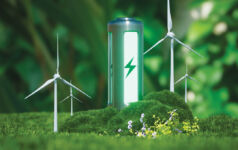 Photo of a green eco-battery surrounded by forestry and windturbines.