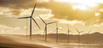 Turbines along the shoreline glowing in evening sunset light, dramatic coastal atmosphere and energy