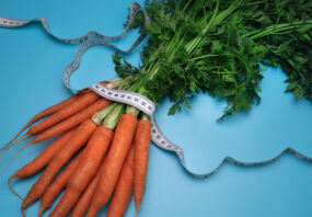 Carrots and measuring tape on the blue background. The concept of diet. Top view, flat lay. Overeating control, diet, nutritionist.
