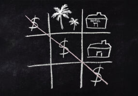 A game of naughts and crosses on a blackboard, but with dollar signs making a diagonal, with a picture of palm trees and a hotel in other squares