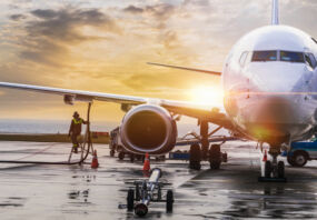 An aeroplane at an airport being refuelled and loaded as the sun sets or rises over the horizon